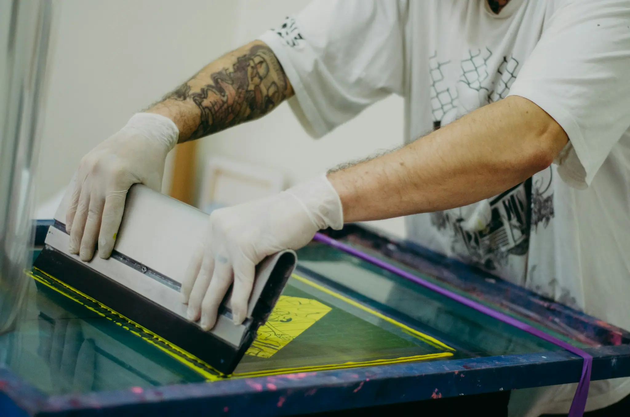 Gloved hands pulling ink across a screen-printing frame