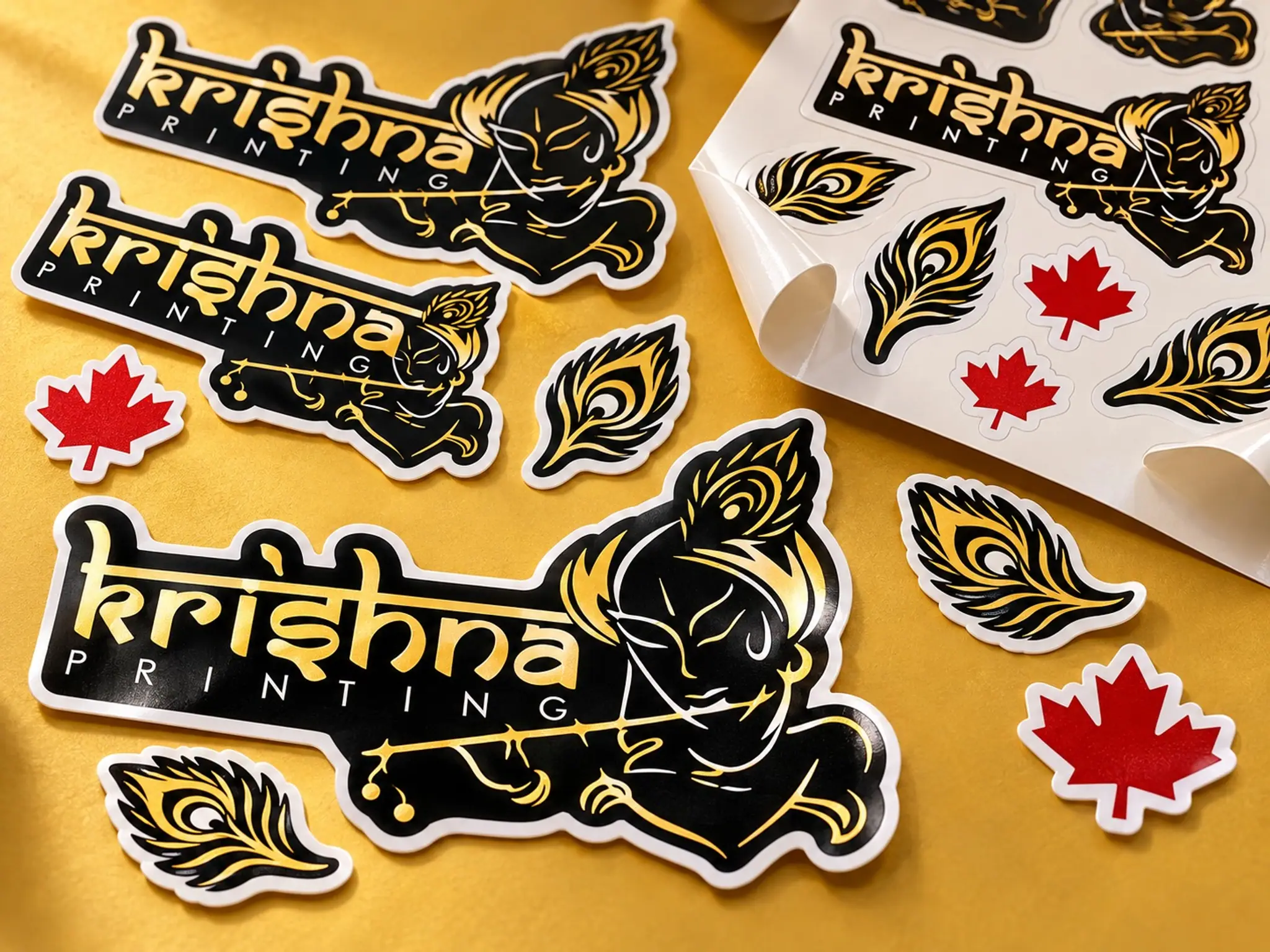 Gold and black die-cut Krishna Printing stickers with peacock-feather and maple-leaf decals