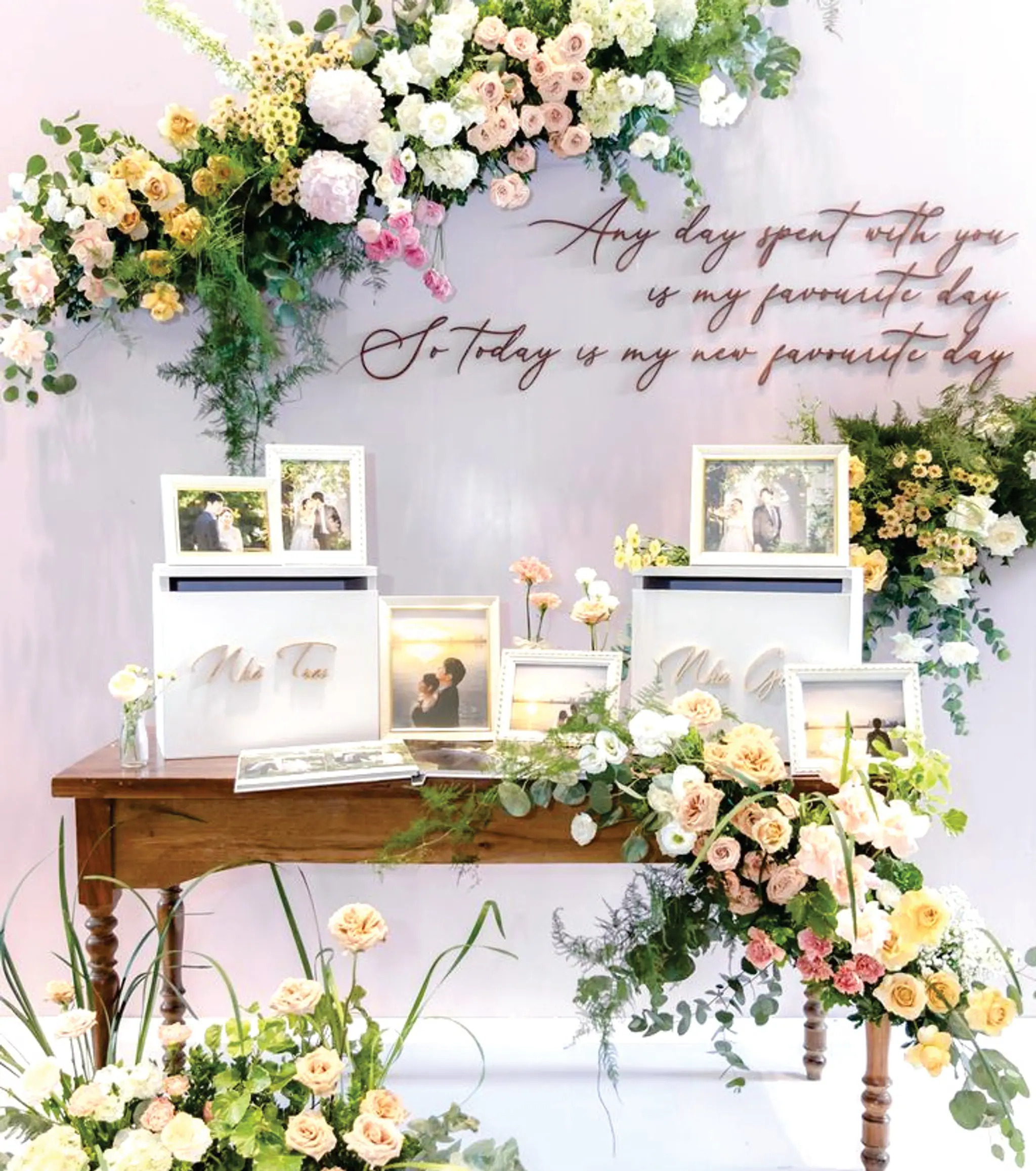 Sweetheart table with framed couple photos and floral arrangements under a gold script wall message