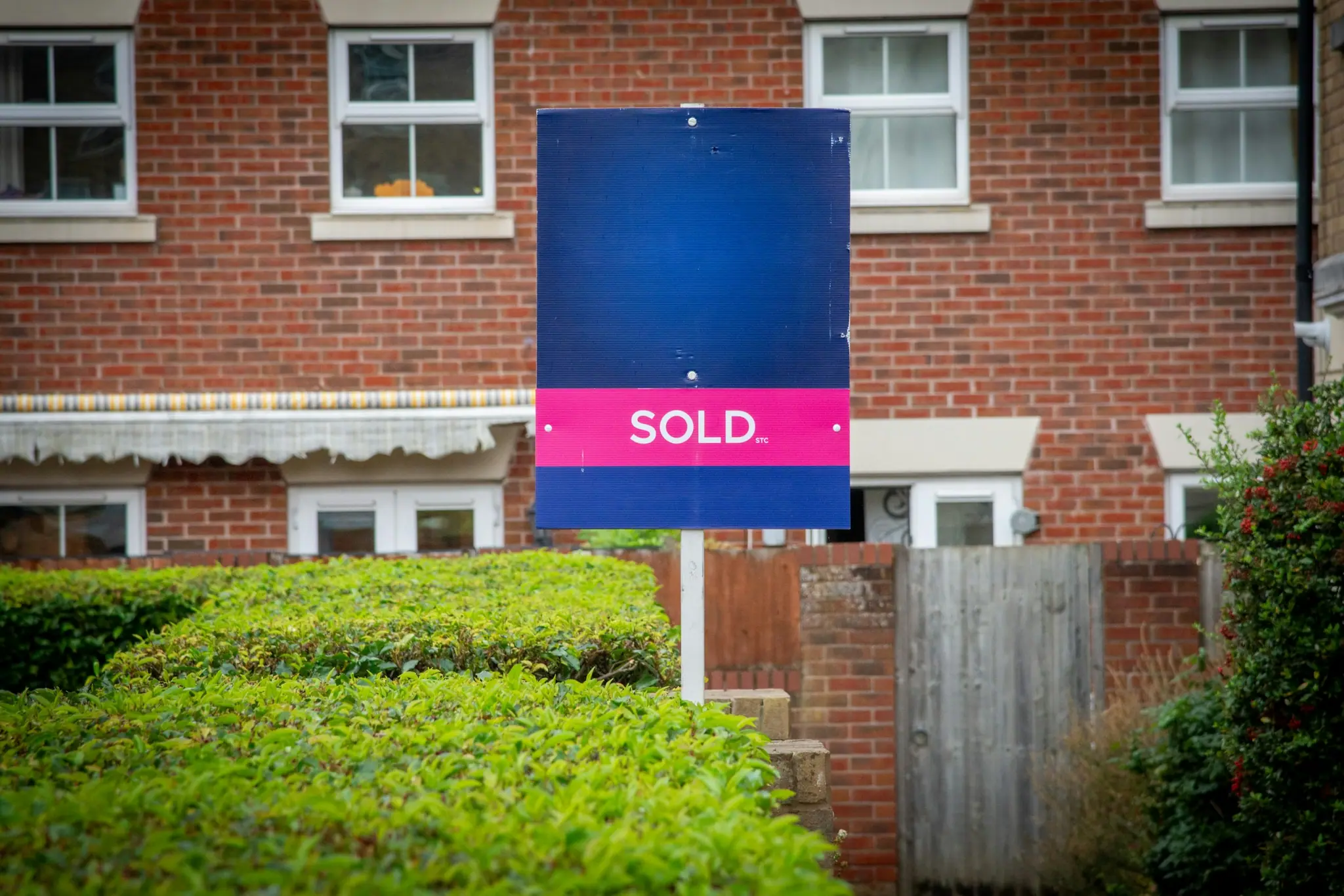 Blue property sign with a pink SOLD rider in front of a brick house